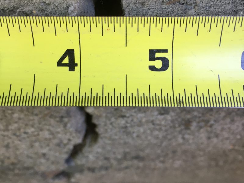 Measuring a concrete crack with a tape measure at half an inch